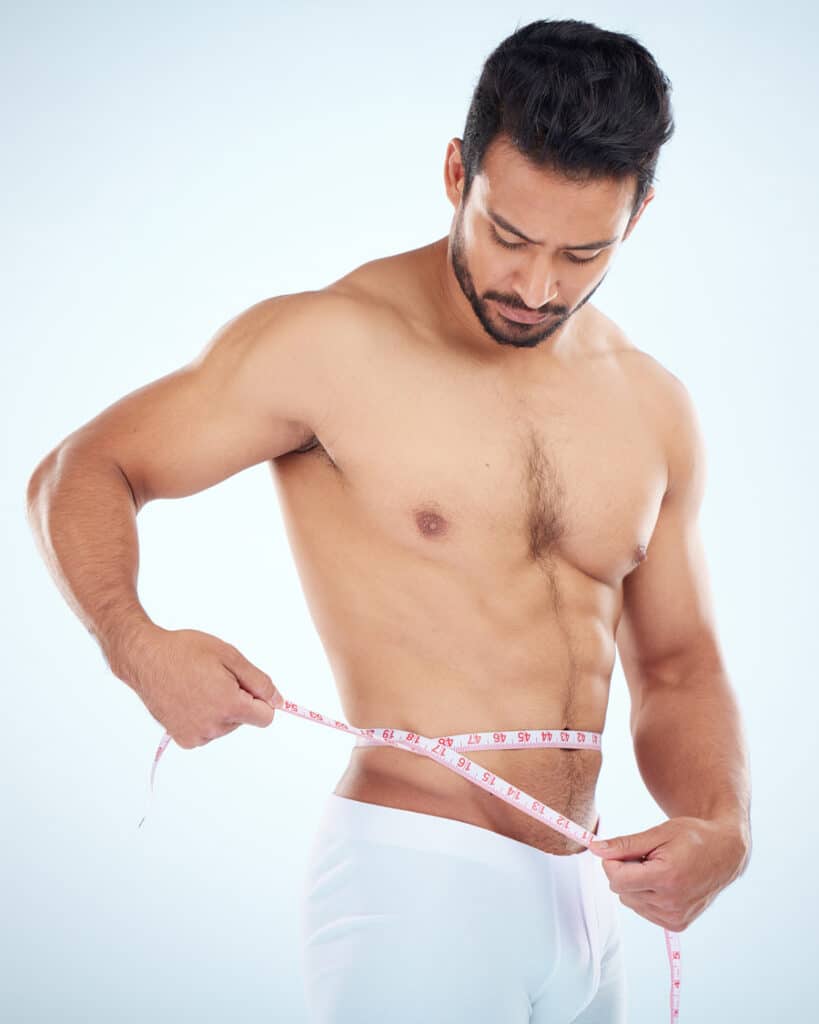 A man measuring his waist with a tape measure.