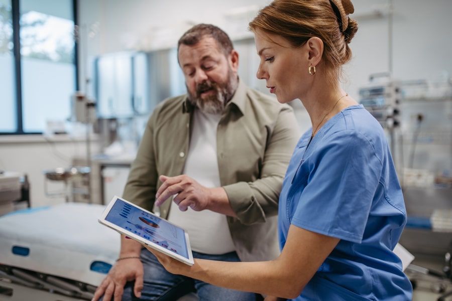 A nurse and a doctor in blue scrubs looking at a tablet screen together in a hospital setting.