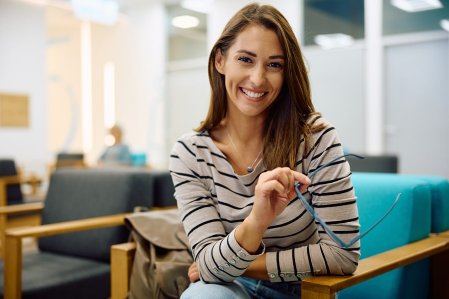A girl with a pleasant expression sits on a couch in a waiting room, exuding happiness.