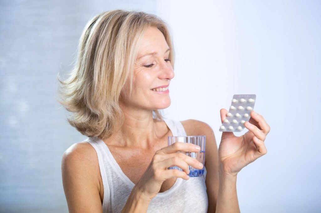 A woman is ready to take a pill, holding it in one hand and a glass of water in the other hand