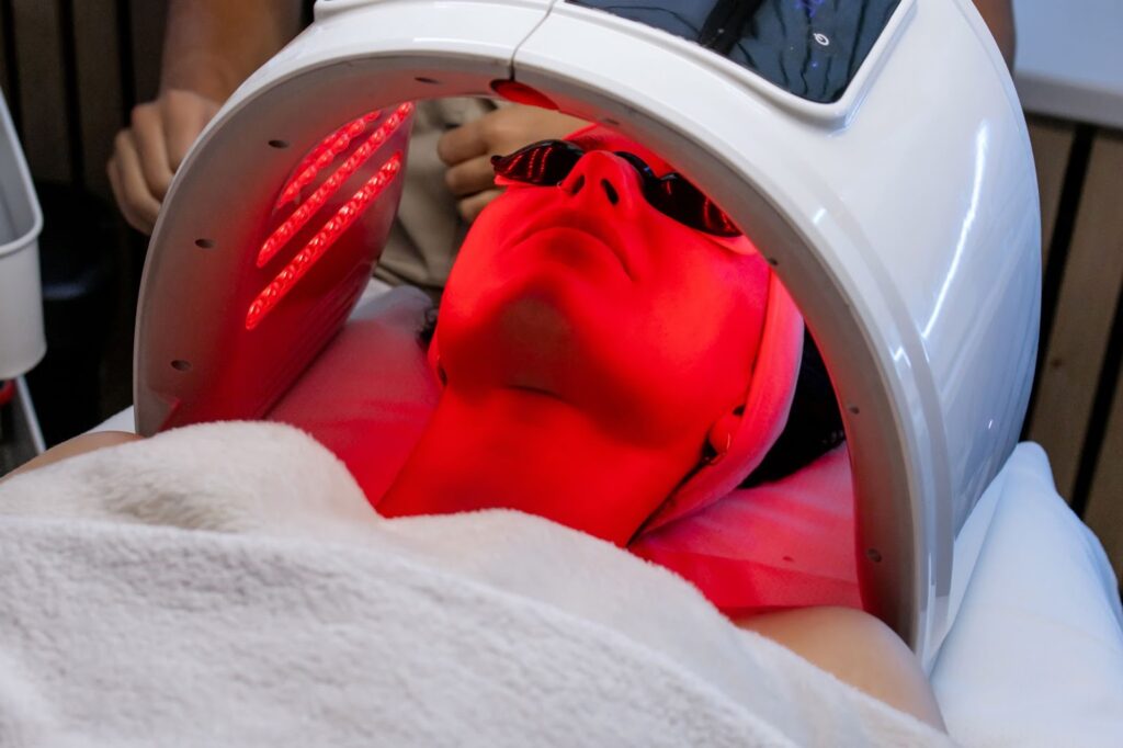 Person receiving red light therapy under a specialized device.