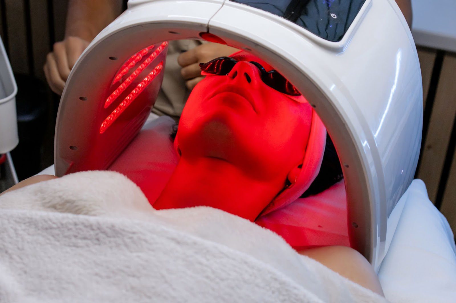 Person receiving red light therapy under a specialized device.