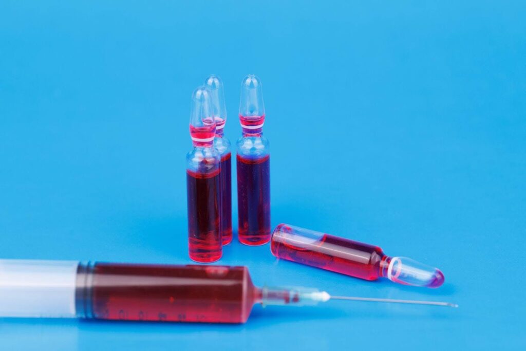 A medical syringe containing red liquid with a visible needle set against a plain backdrop