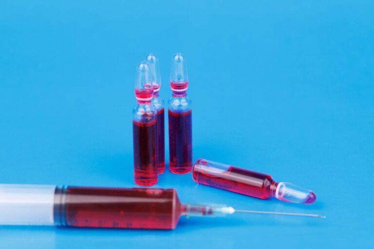 A medical syringe containing red liquid with a visible needle set against a plain backdrop