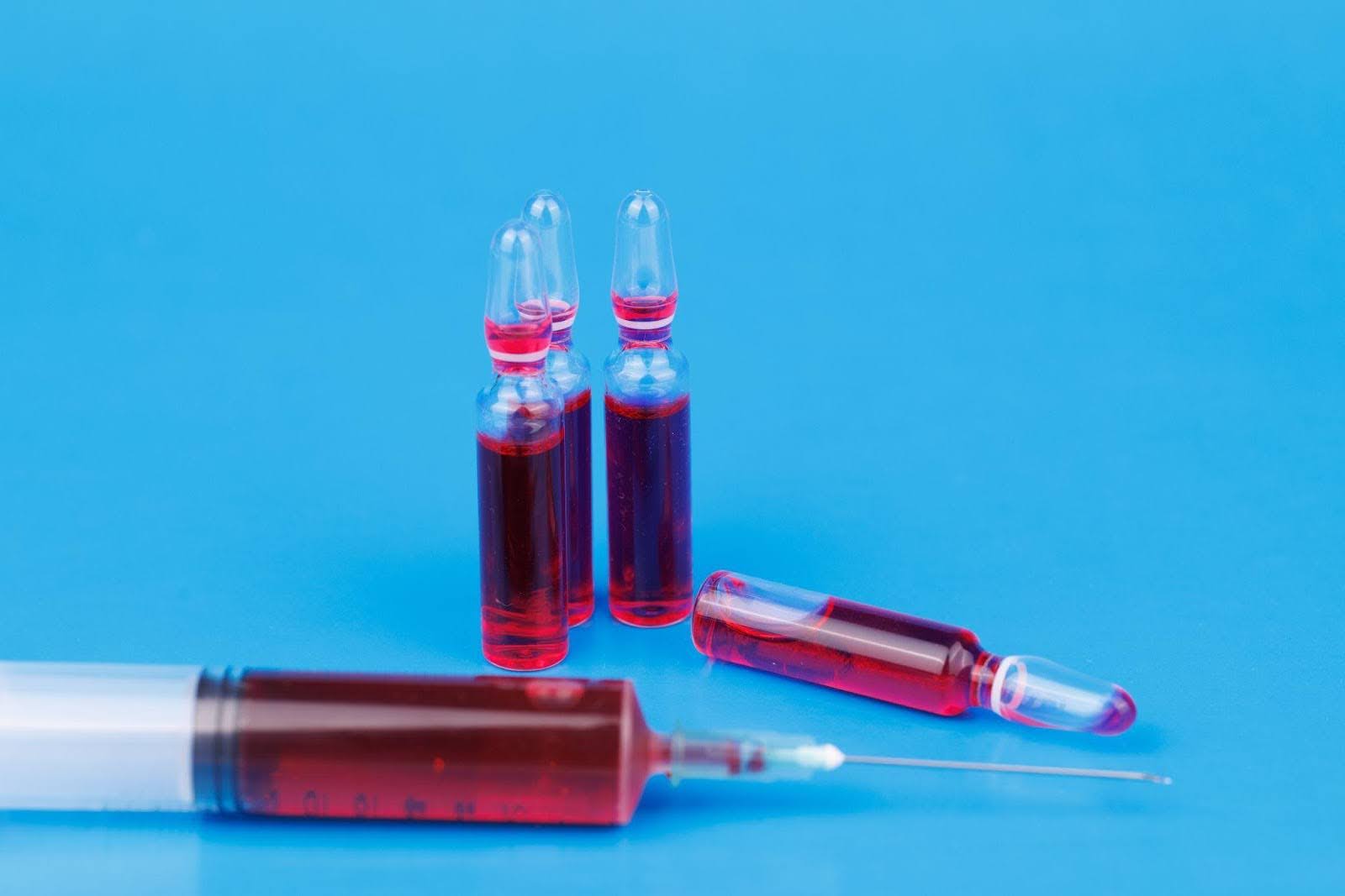 A medical syringe containing red liquid with a visible needle set against a plain backdrop