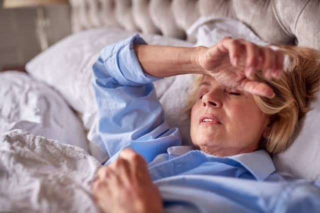 A woman lies in bed with her hands resting on her head appearing relaxed and contemplative