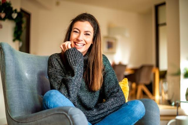 A woman sitting on a couch smiling warmly at the camera exuding a sense of happiness and comfort