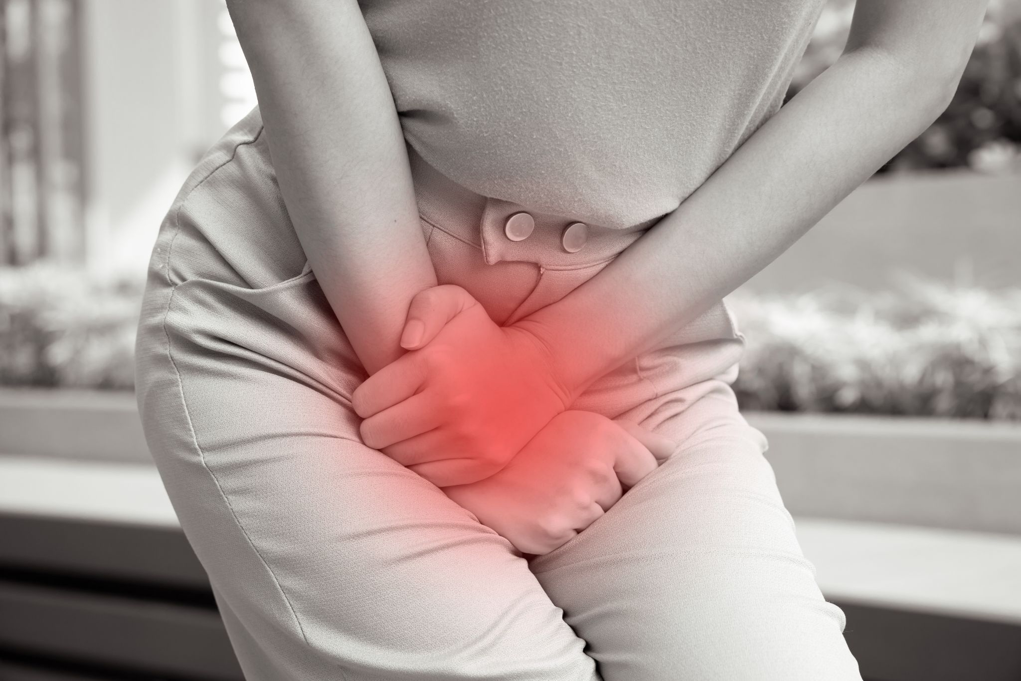 A black and white image of a person holding their lower abdomen with a highlighted red glow indicating pelvic pain or discomfort.
