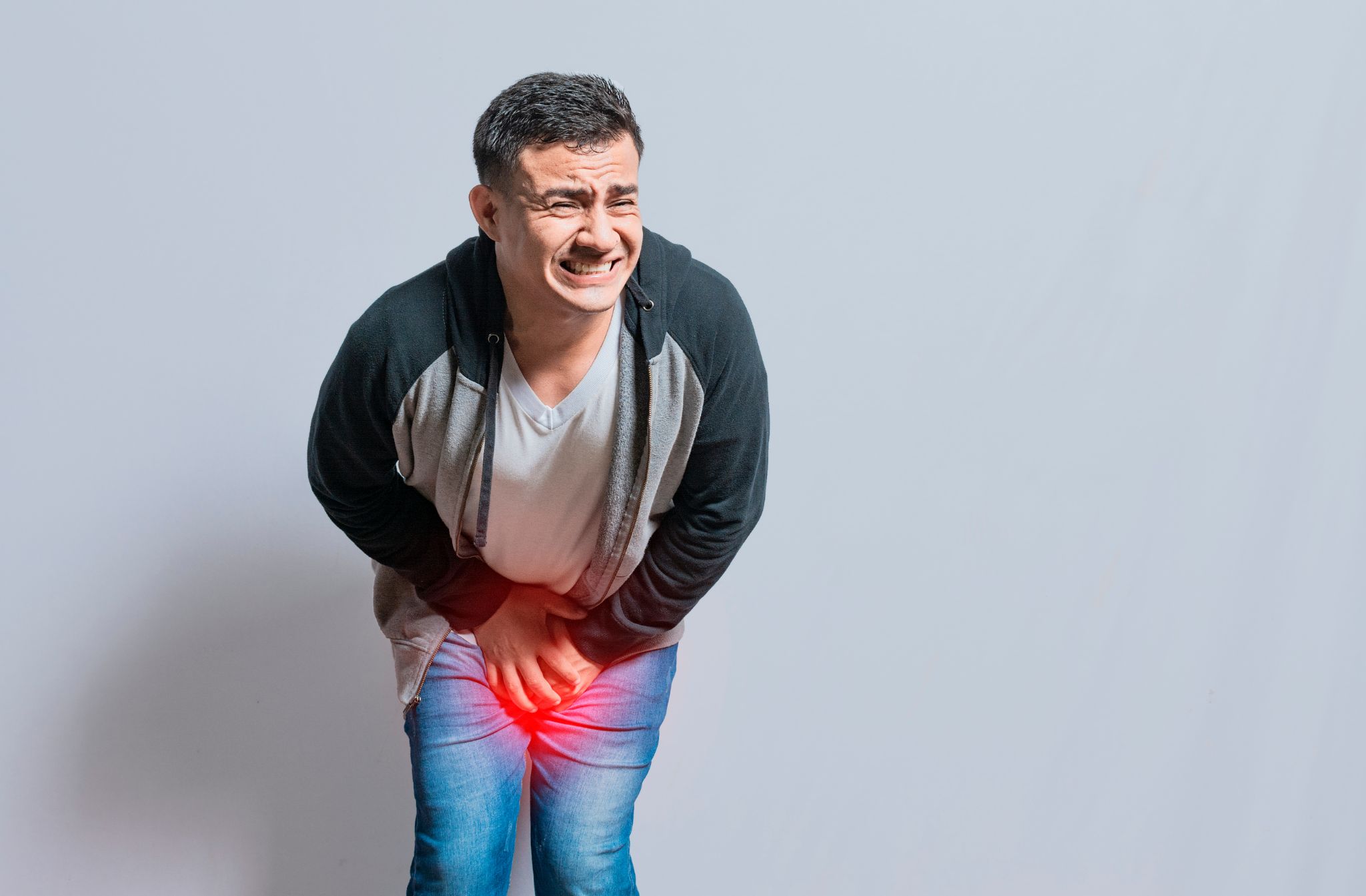 A man grimacing and clutching his groin area with a highlighted red glow indicating severe pelvic pain or injury.