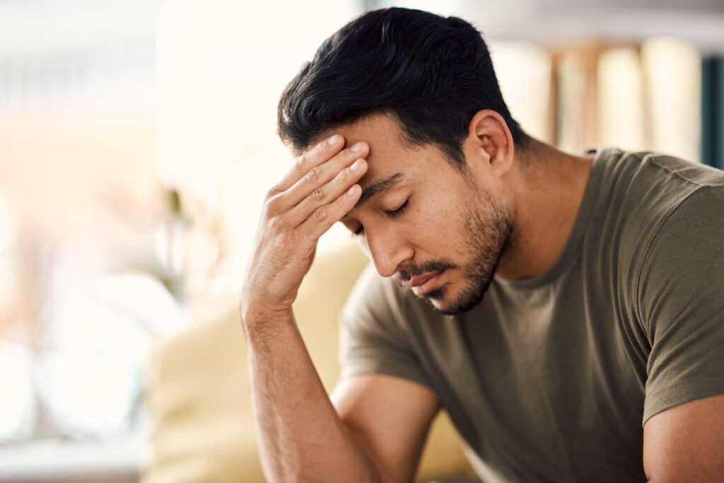 A man on a couch holds his head suggesting feelings of stress or contemplation