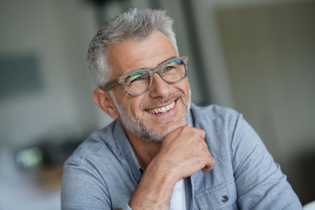A smiling man with glasses is looking directly at the camera