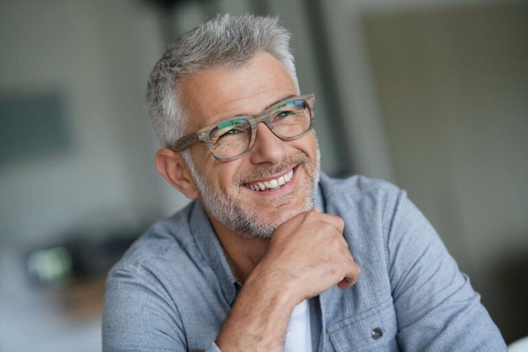 A smiling man with glasses is looking directly at the camera