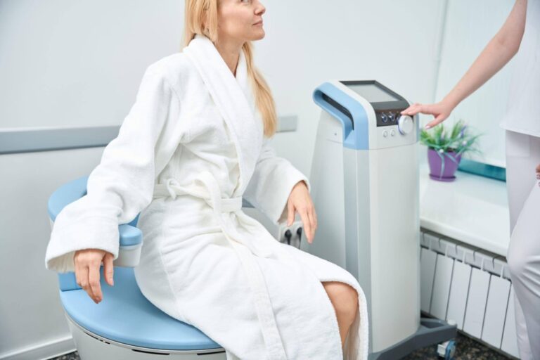 A woman in a bathrobe sits on a chair facing a machine appearing relaxed and contemplative