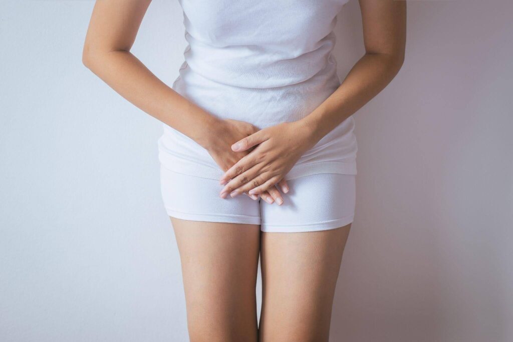 Cropped person in white clothing holds their lower abdomen with both hands