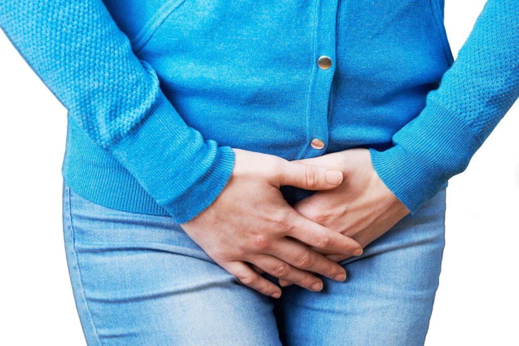 Person in a blue sweater and jeans clutches their lower abdomen with both hands